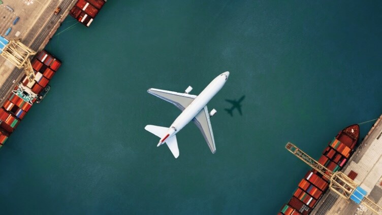 Ein Flugzeug fliegt über dem Wasser und sein Schatten ist auf dem Wasser zu sehen; rote Türen sind geschlossen