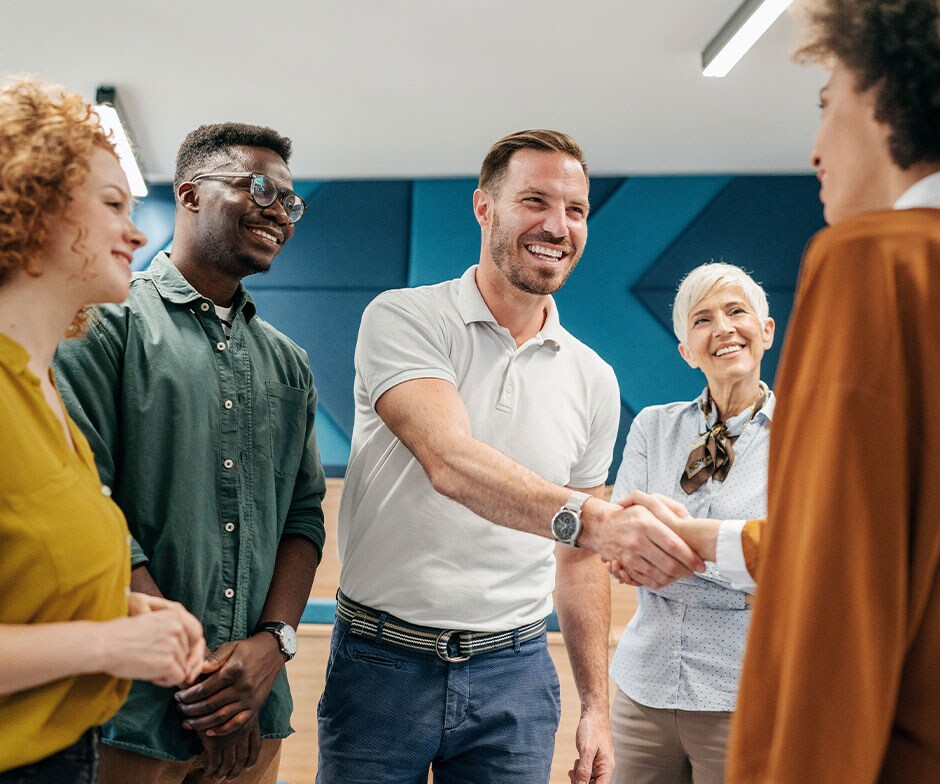 Gruppe stehender Menschen, von denen sich zwei die Hand geben