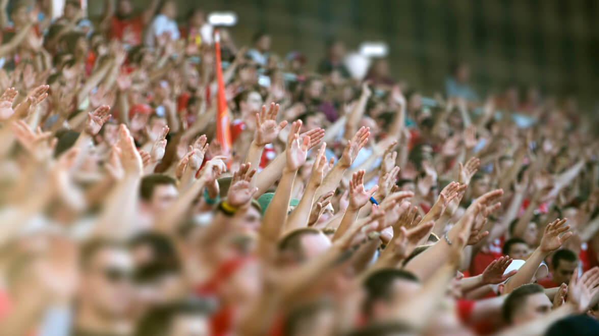 Große Menge begeisterter Fans, die bei einer Stadionveranstaltung gleichzeitig die Hände heben.