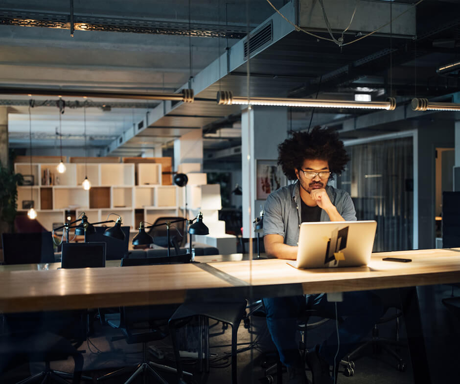 Eine Person sitzt an einem Schreibtisch und hat einen Laptop vor sich.
