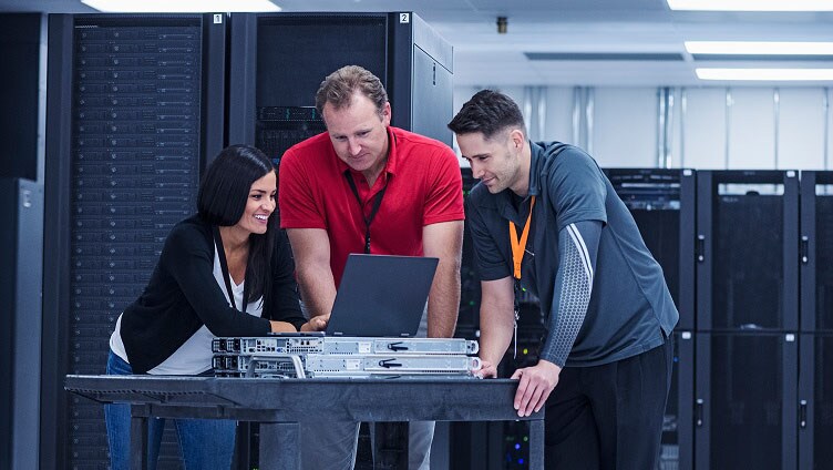 Grupo revisando el hardware del servidor y el portátil en una sala de servidores de alta tecnología.