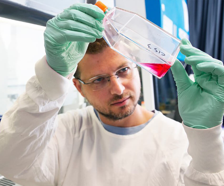 person wearing gloves and lab coat looking at fluid