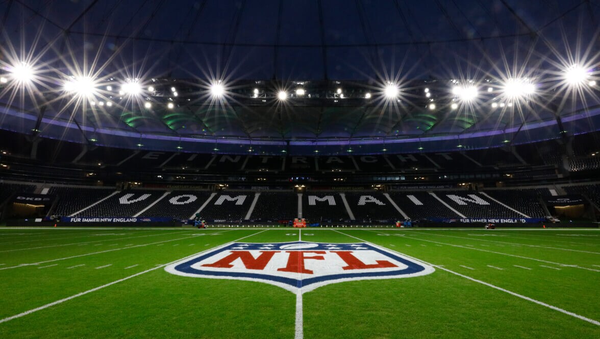 Logo de la NFL au centre d’un terrain à l’intérieur d’un stade illuminé.