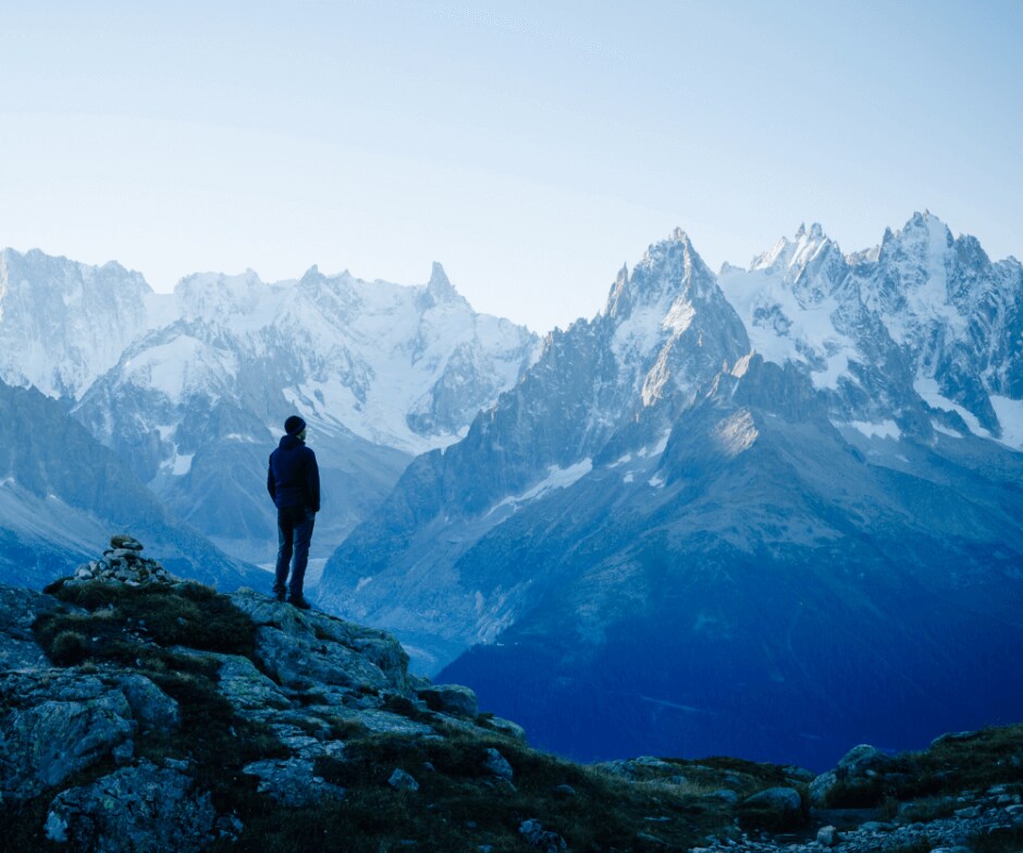 person standing on cliff admiring the mountain ridges