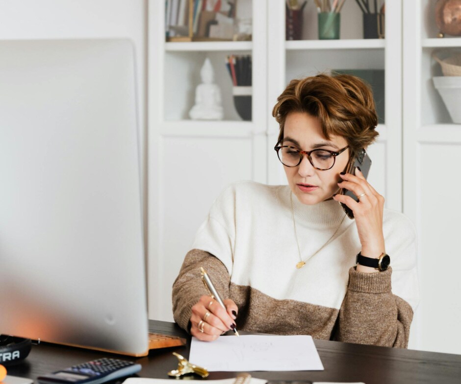 Une personne parle sur son smartphone tout en prenant des notes à un bureau dans un environnement de bureau à domicile moderne.
