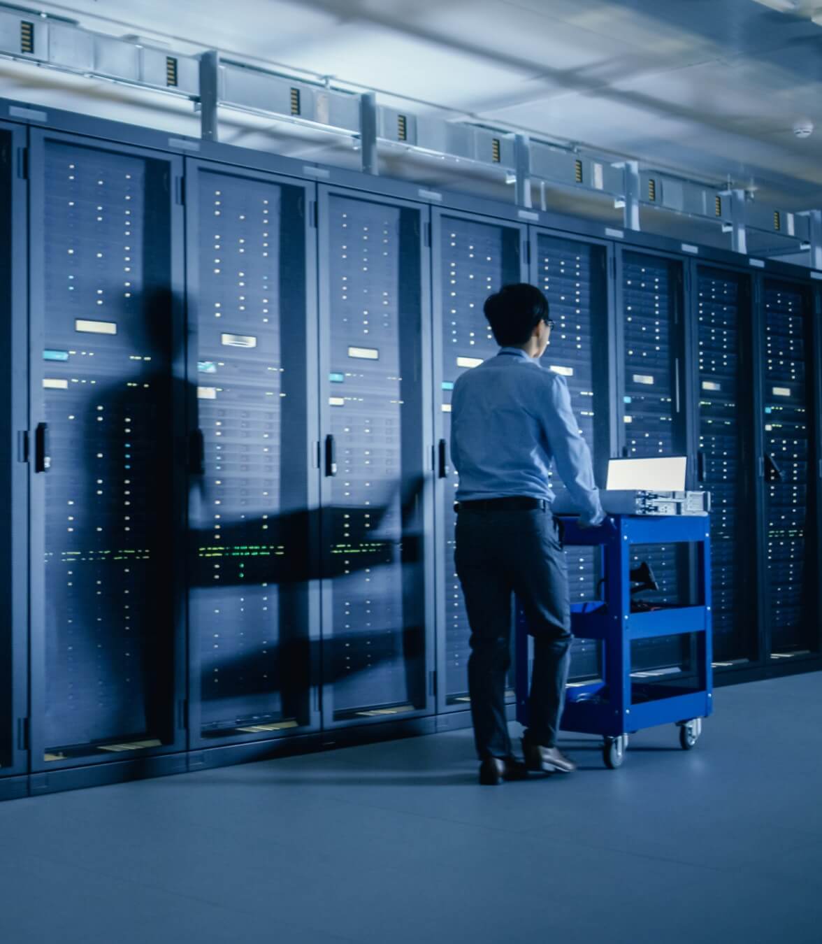 Une personne se tient dans l'allée d'un data center et travaille avec des équipements devant de grands racks de serveurs.