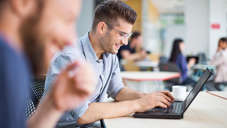 Persona che lavora su un laptop in un moderno ambiente d'ufficio con una tazza di caffè sulla scrivania.