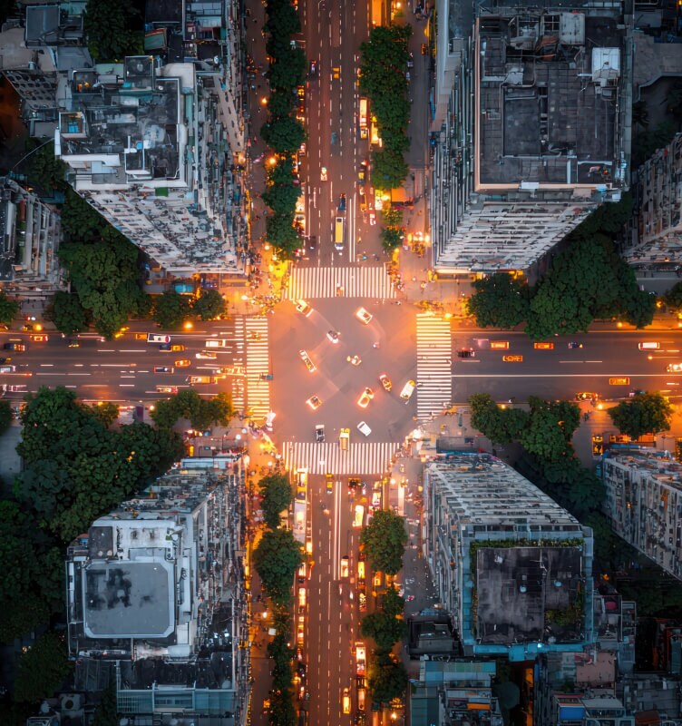 Incrocio cittadino visto dall'alto di notte con edifici illuminati e traffico.