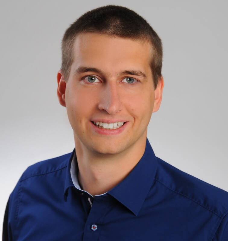 Professional headshot of a person wearing a blue collared shirt against a plain background.