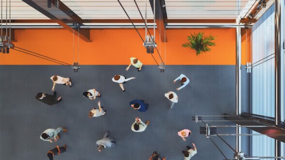 Top‑down view of employees walking through a modern office lobby with bright orange flooring.
