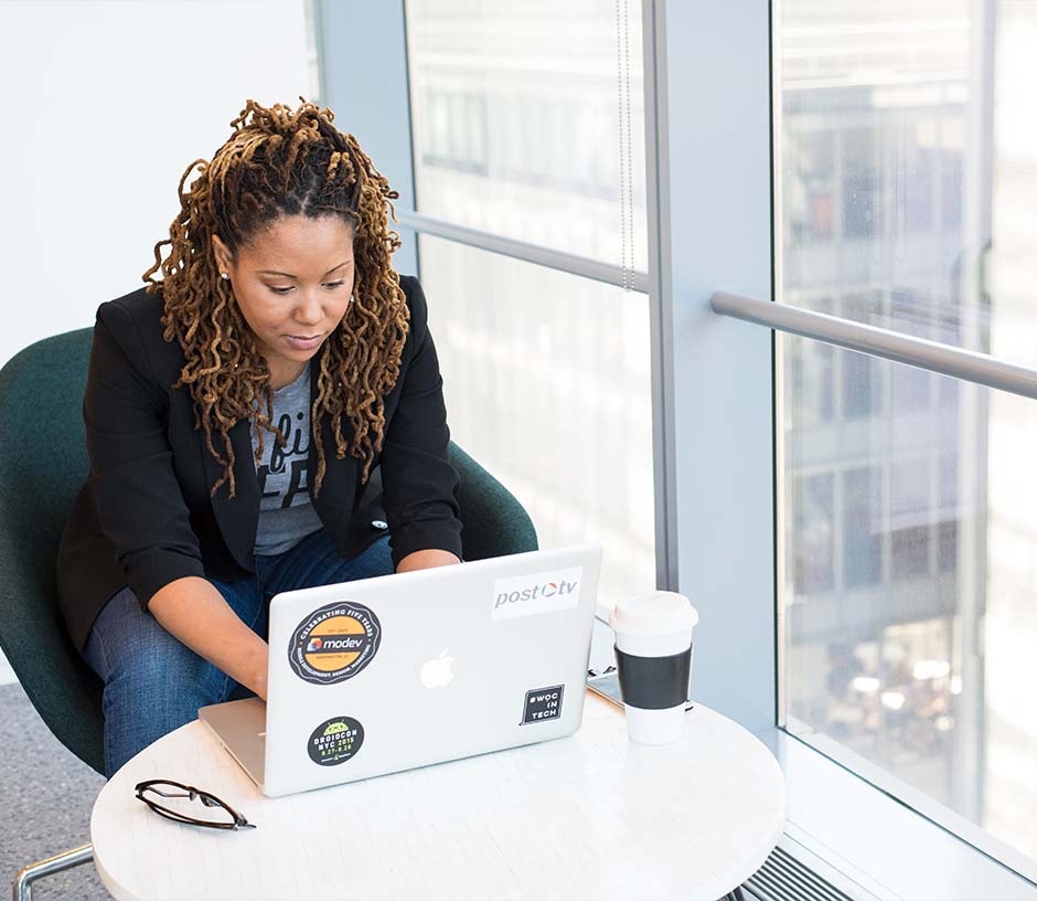 lady working on laptop at small table beside high-rise window overlooking the city