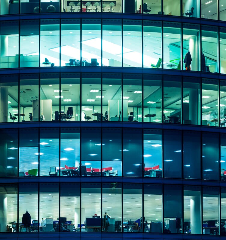 Exterior view of a modern office building with illuminated interior floors at night.