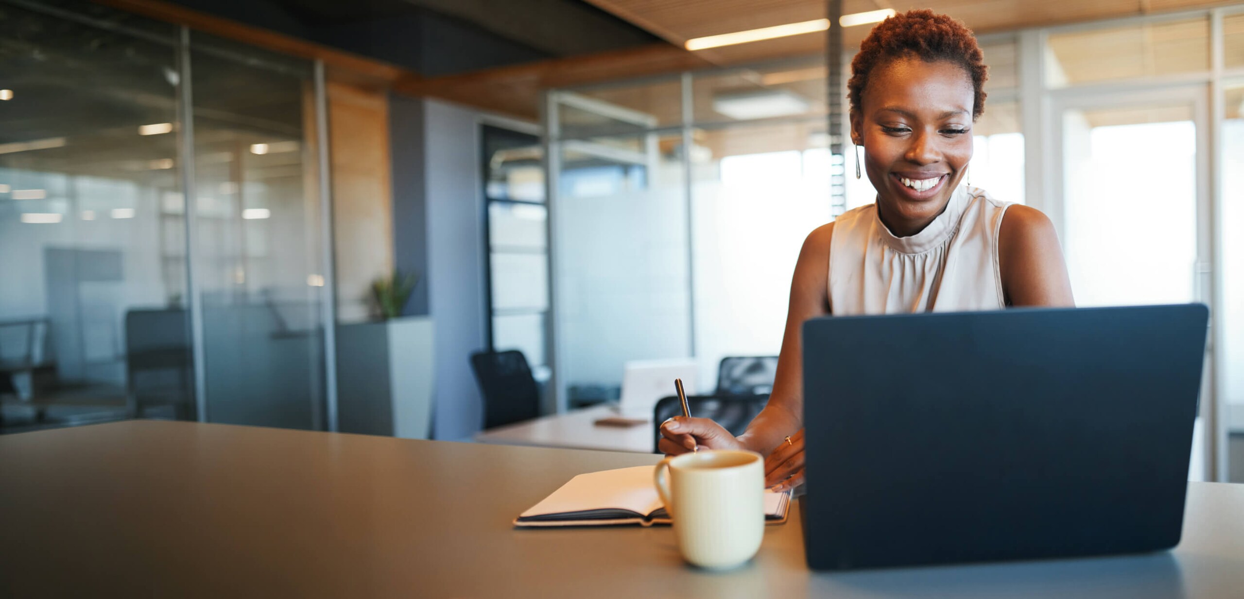 A Person in front of laptop sitting and writing in a book