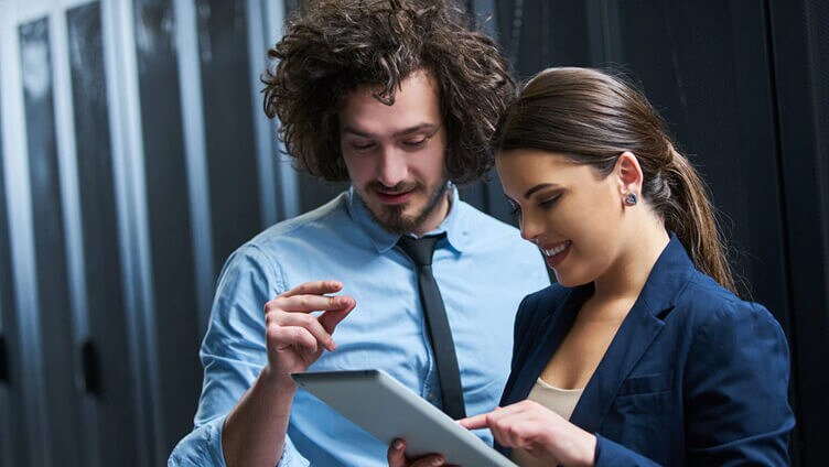 Two professionals reviewing information on a tablet inside a technology server room.