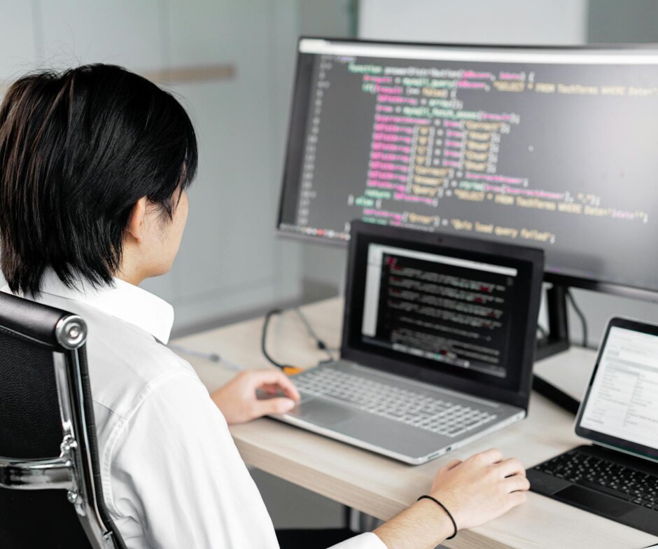 Person working at a desk with multiple monitors displaying programming code.