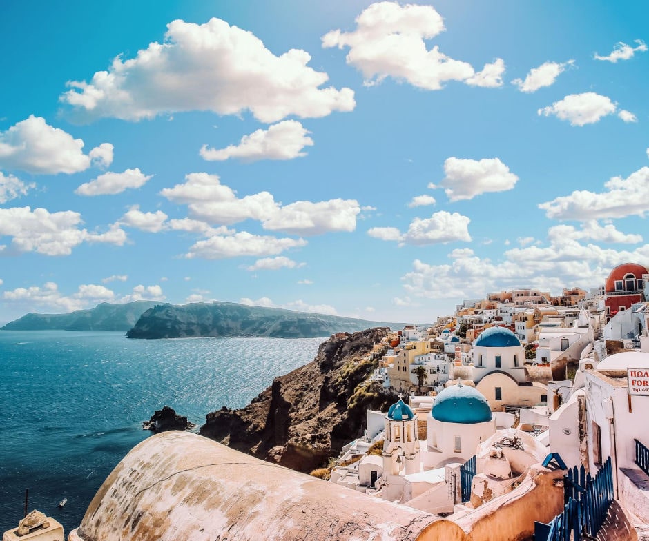 Panoramic view of Santorini’s whitewashed houses with blue-domed churches overlooking the Aegean Sea under a bright blue sky