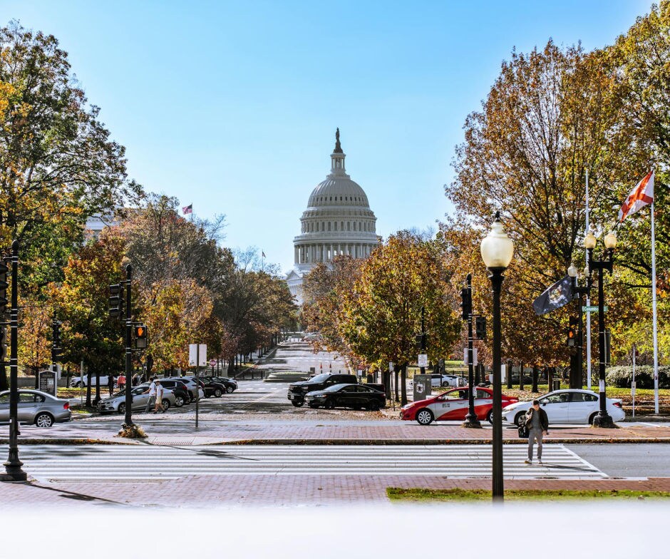 Scenic view of the United States Capitol building framed by autumn trees and street with cars and flags