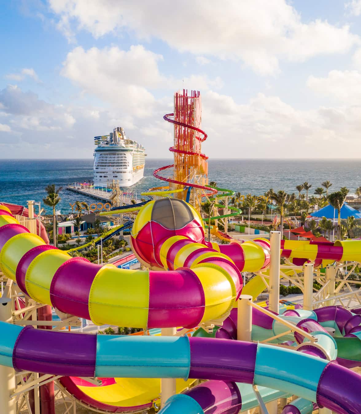 Colorful waterpark slides overlooking the ocean with a docked cruise ship in the background.