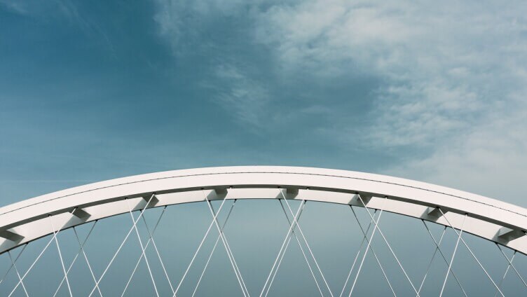A modern white arch bridge set against a lightly clouded blue sky.