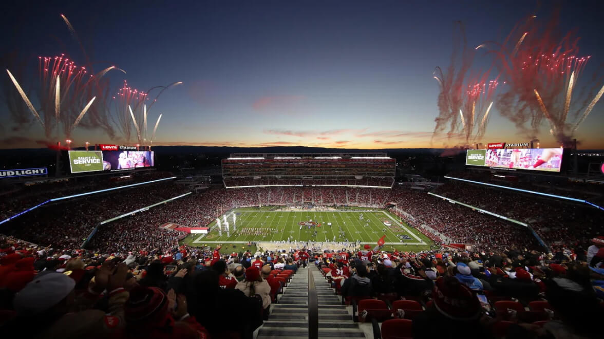 Football stadium at sunset with fireworks lighting the sky during a game.