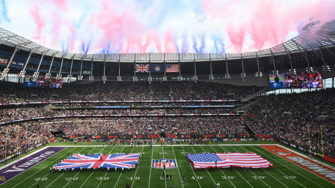 Full stadium during an NFL London game with giant UK and US flags displayed on the field.