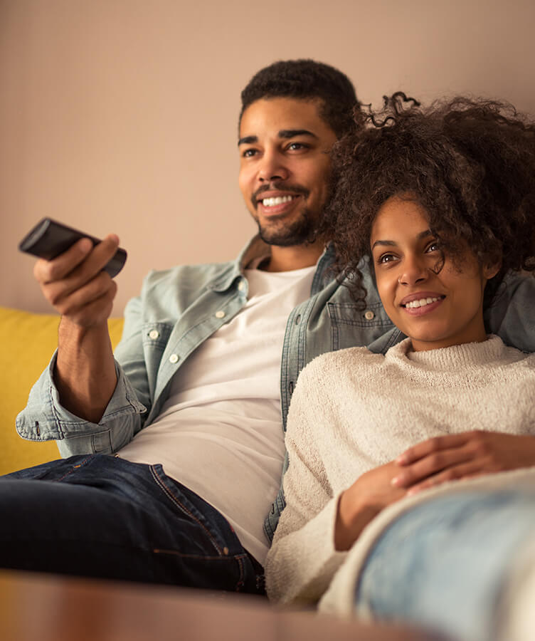 two people sitting in couch comfortable and watching tv with one person holding remote