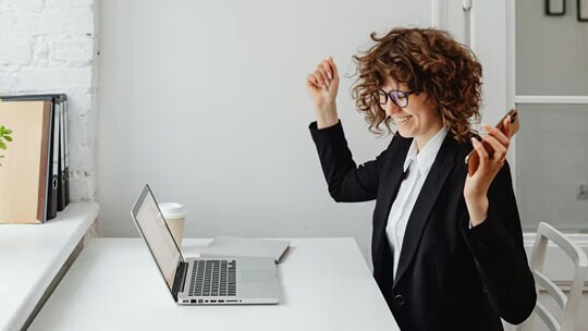 Profissional de negócios em uma mesa usando um laptop e segurando um telefone enquanto gesticula durante o trabalho.