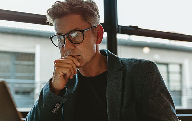 homem com óculos pretos olhando para laptop pensivamente