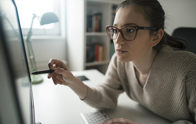 mulher com óculos usando uma caneta como um ponteiro em direção ao monitor