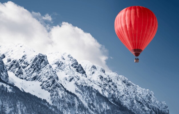 red hot air balloon floating over snow capped mountains