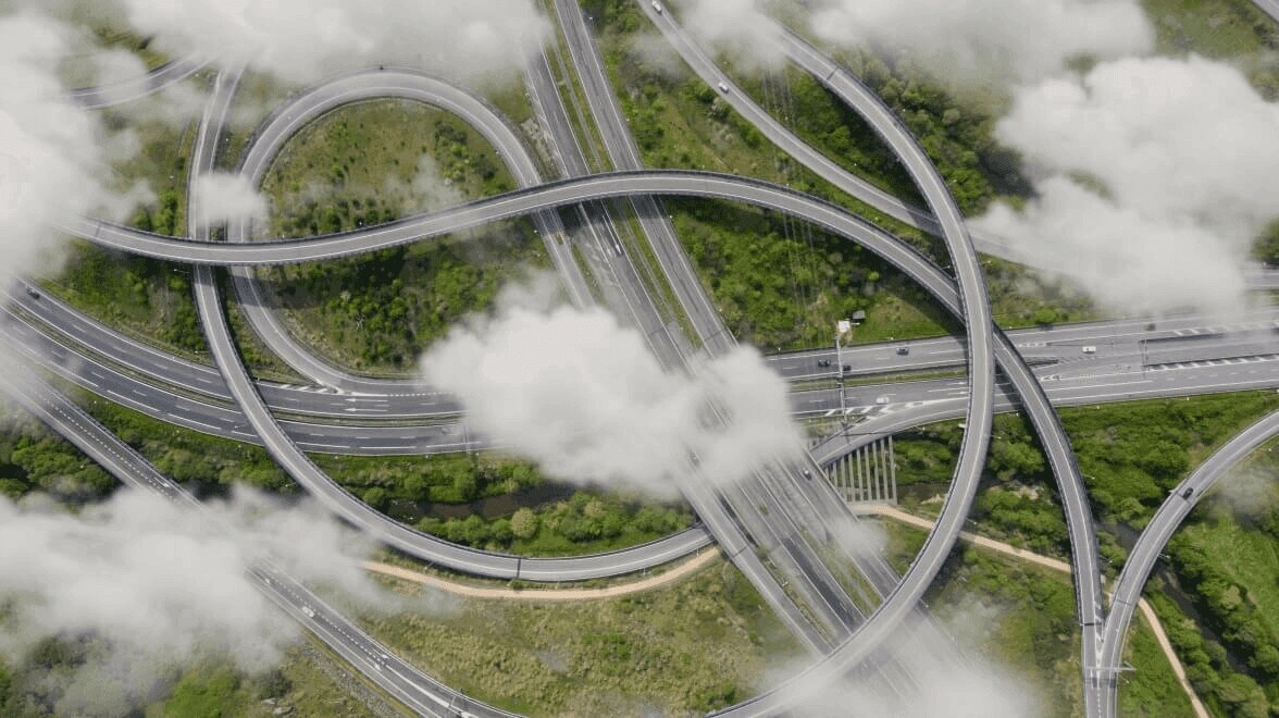 Aerial view of a large multi‑level highway interchange winding through green landscape and low clouds.